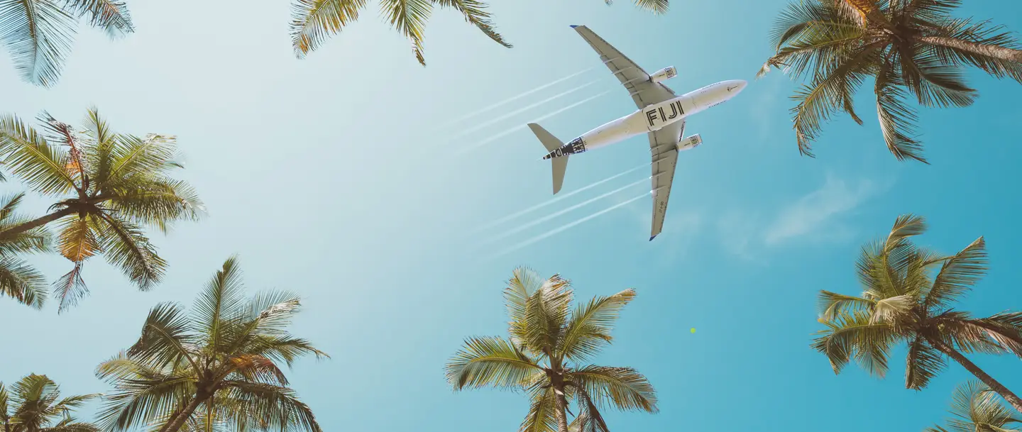 Fiji Airways flies over palm trees against a bright blue sky